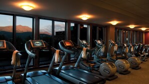 Une salle de sport équipée de tapis de course et d’appareils elliptiques, de grandes fenêtres offrant une vue sur les montagnes et d’appareils d’exercice dotés d’écrans numériques.