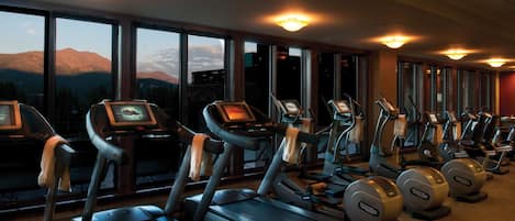 Un gimnasio con cintas de correr y máquinas elípticas, amplias ventanas con vistas a la montaña y equipamiento de ejercicio con pantallas digitales.