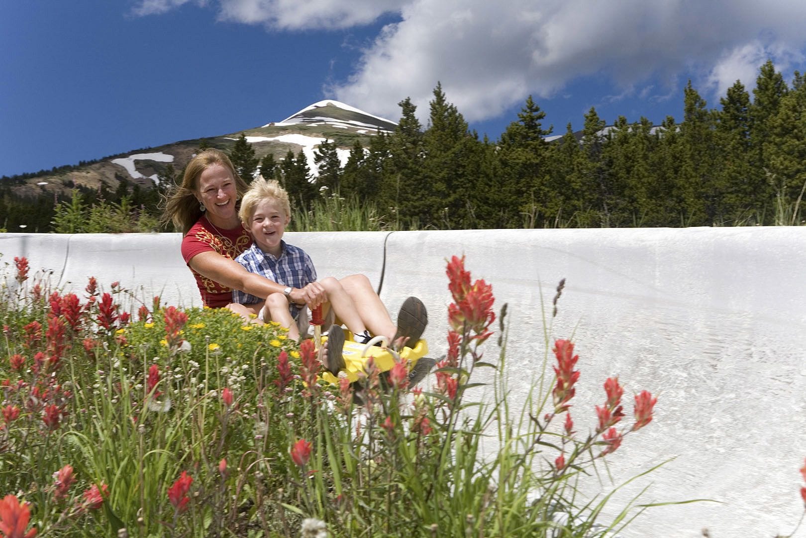 Une personne et un enfant sur une piste de luge, dans un environnement naturel, avec une montagne en arrière-plan.