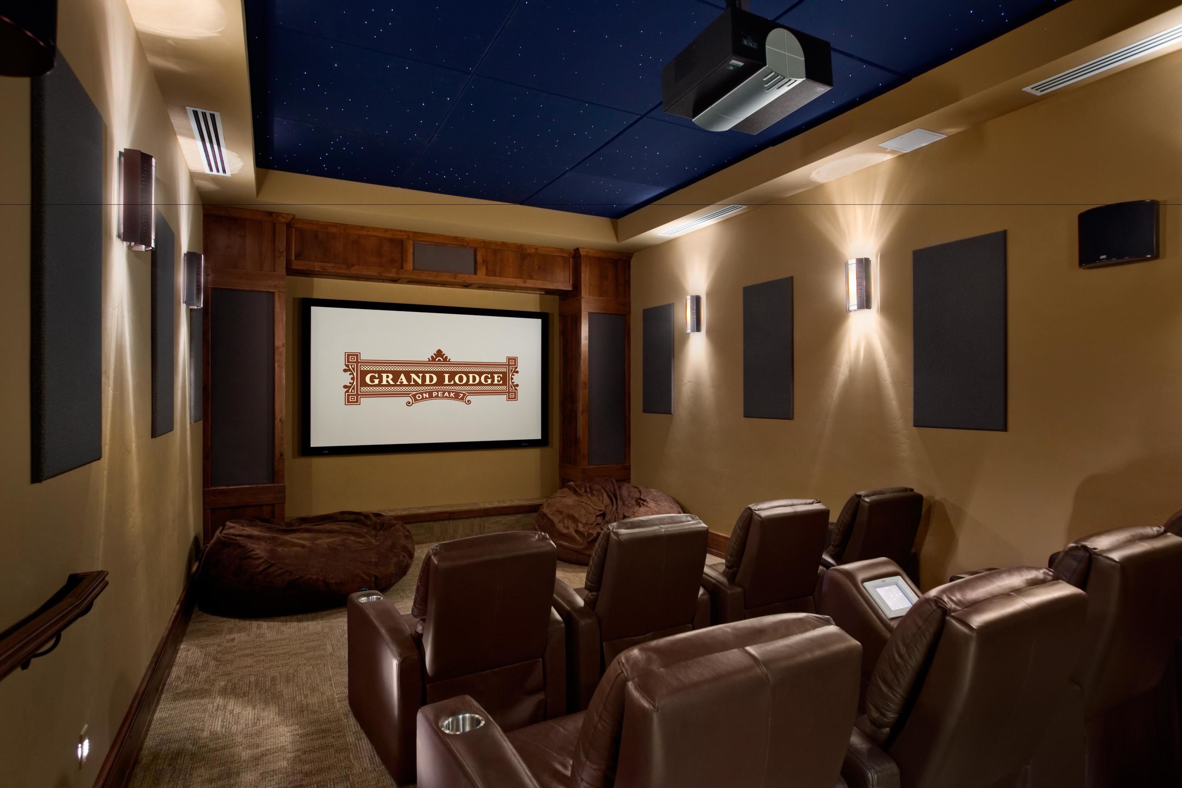A home theater room with a starry ceiling, a screen displaying "Grand Lodge on the Peak," and leather recliners.