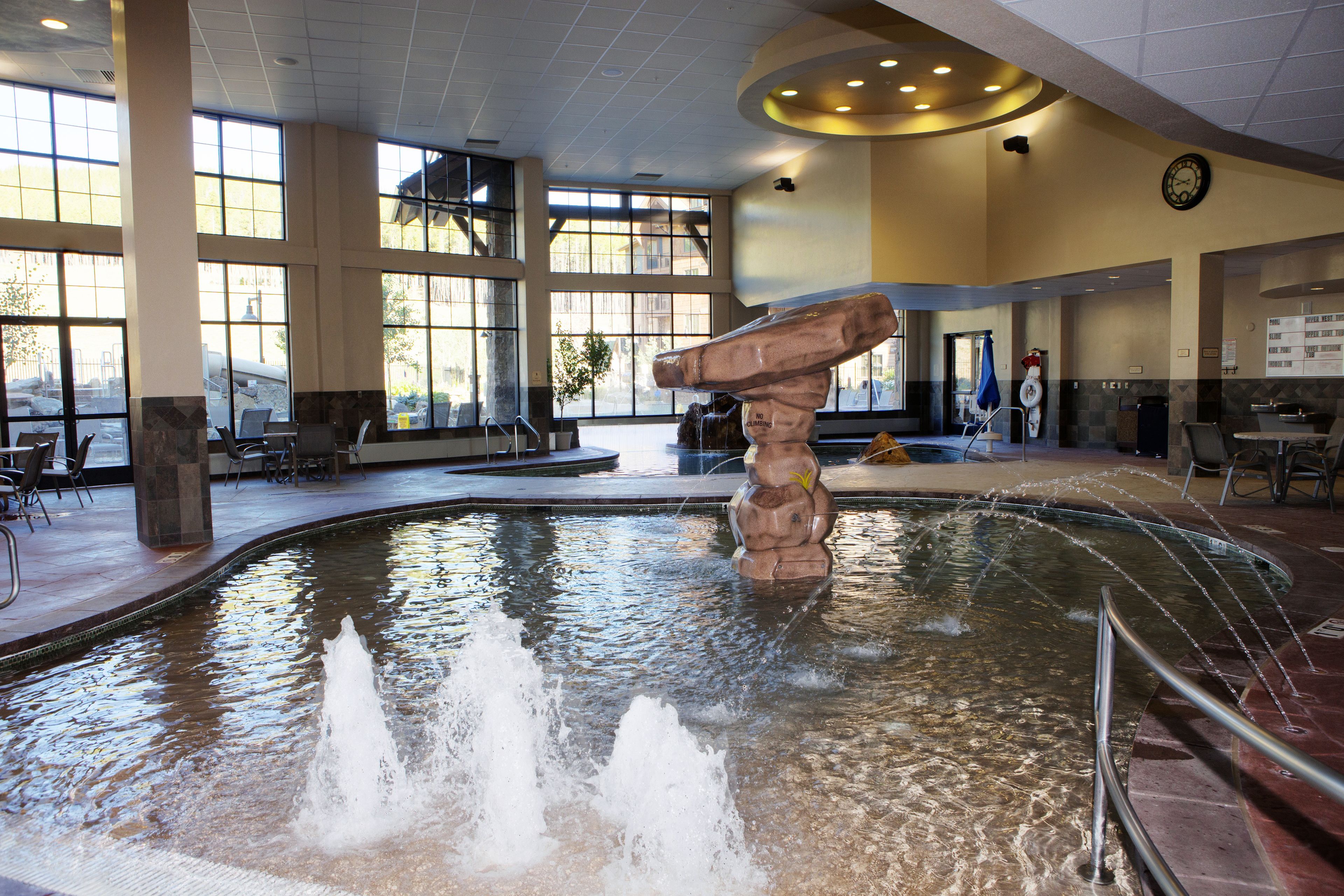 A spacious indoor pool area with a central rock feature and multiple seating areas around the pool.