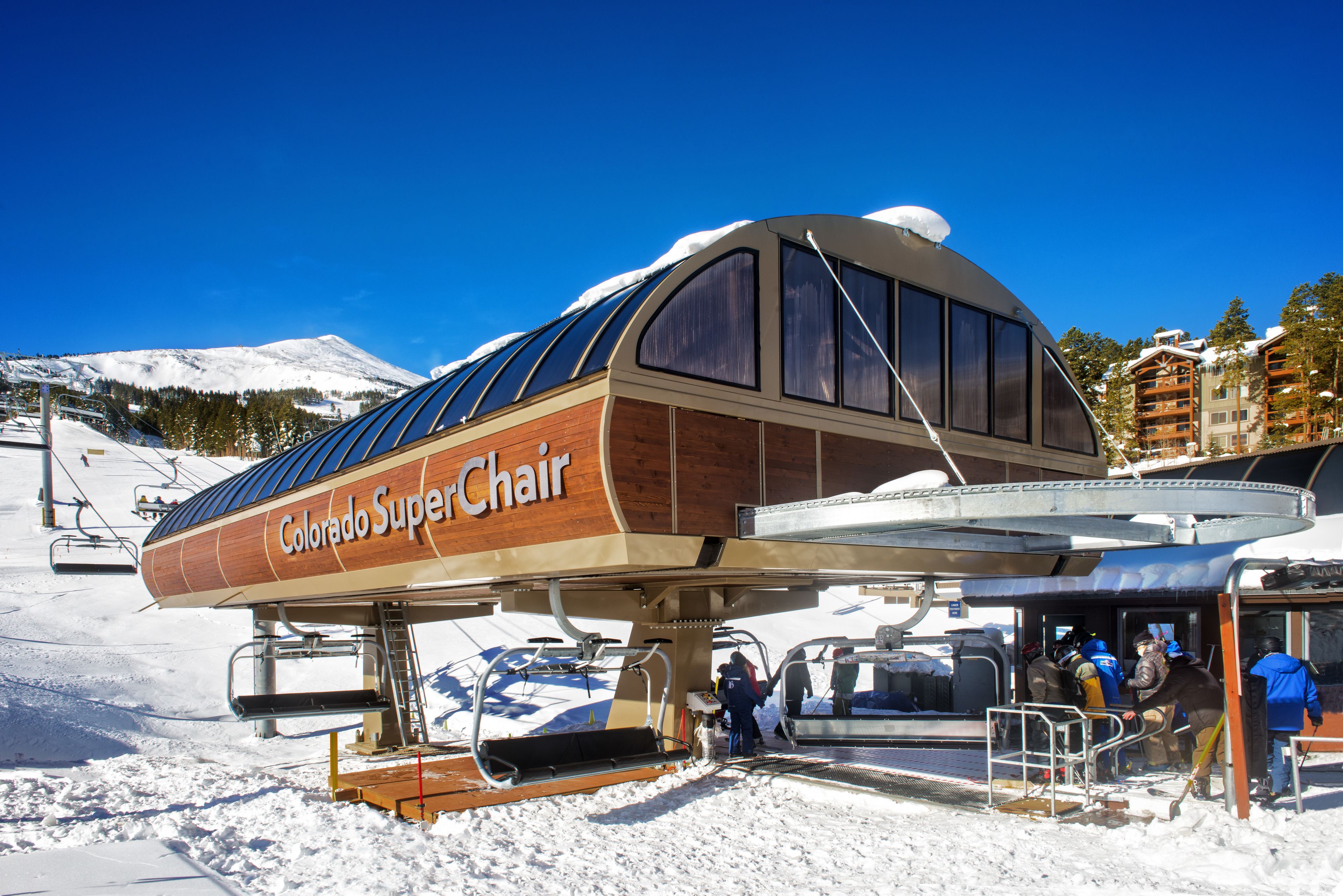 Une télésiège en bois, avec l’inscription « Colorado SuperChair » sur le côté, se détache sur le fond d’une montagne enneigée.