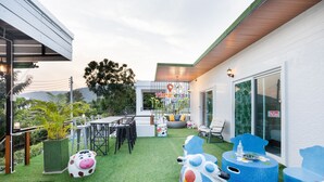 A modern outdoor patio with artificial grass, a dining area with chairs and tables, and colorful cow-shaped seating. - Timeless Pool Villa Huahin (Hua Hin)