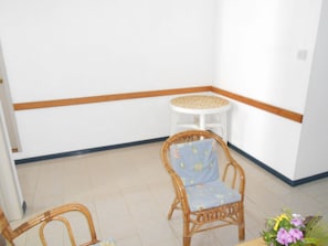 Quarto de canto com uma cadeira de vime, uma mesa redonda pequena e um arranjo floral.