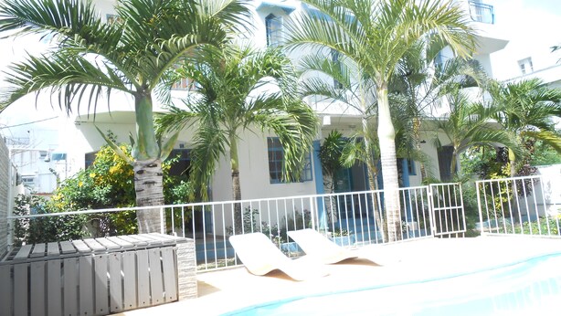 A pool area with lounge chairs, palm trees, and a white building with blue accents. - Aquatic Villa Grand Baie Mauritius (Grand-Baie)