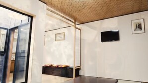A modern room with a large window, a flat-screen TV, and a small wooden cabinet with cushions.