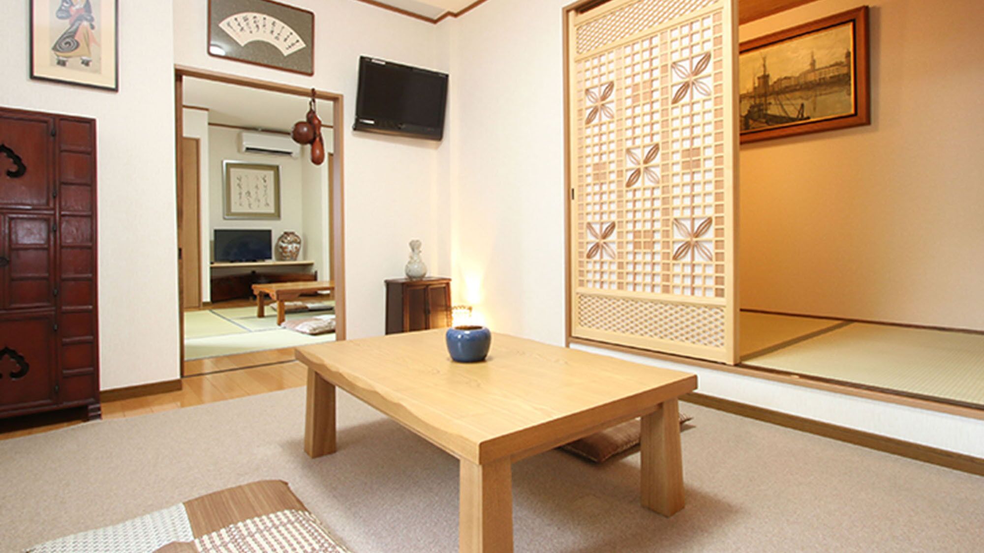 Una habitación japonesa tradicional con suelo de tatami, una mesa de madera baja, un jarrón azul y un celosía de papel shoji.