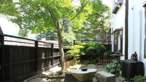 A traditional Japanese garden with a wooden fence, stone lanterns, and a variety of plants.