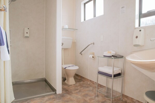A bathroom with a toilet, a glass shelf with towels, a sink, and a shower area.