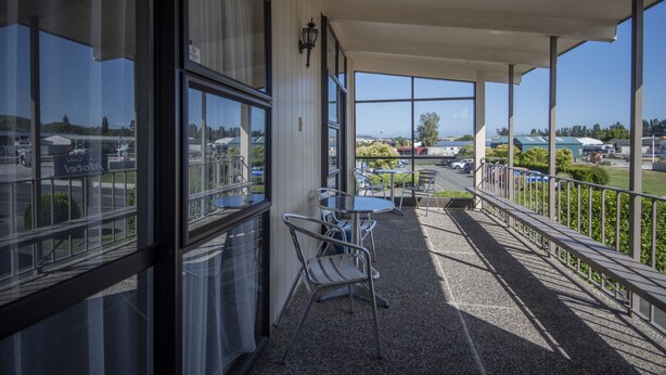 A covered outdoor area with metal chairs and tables, large windows, and a view of a parking lot and buildings. - Tuki Tuki Motel (Waipukurau)