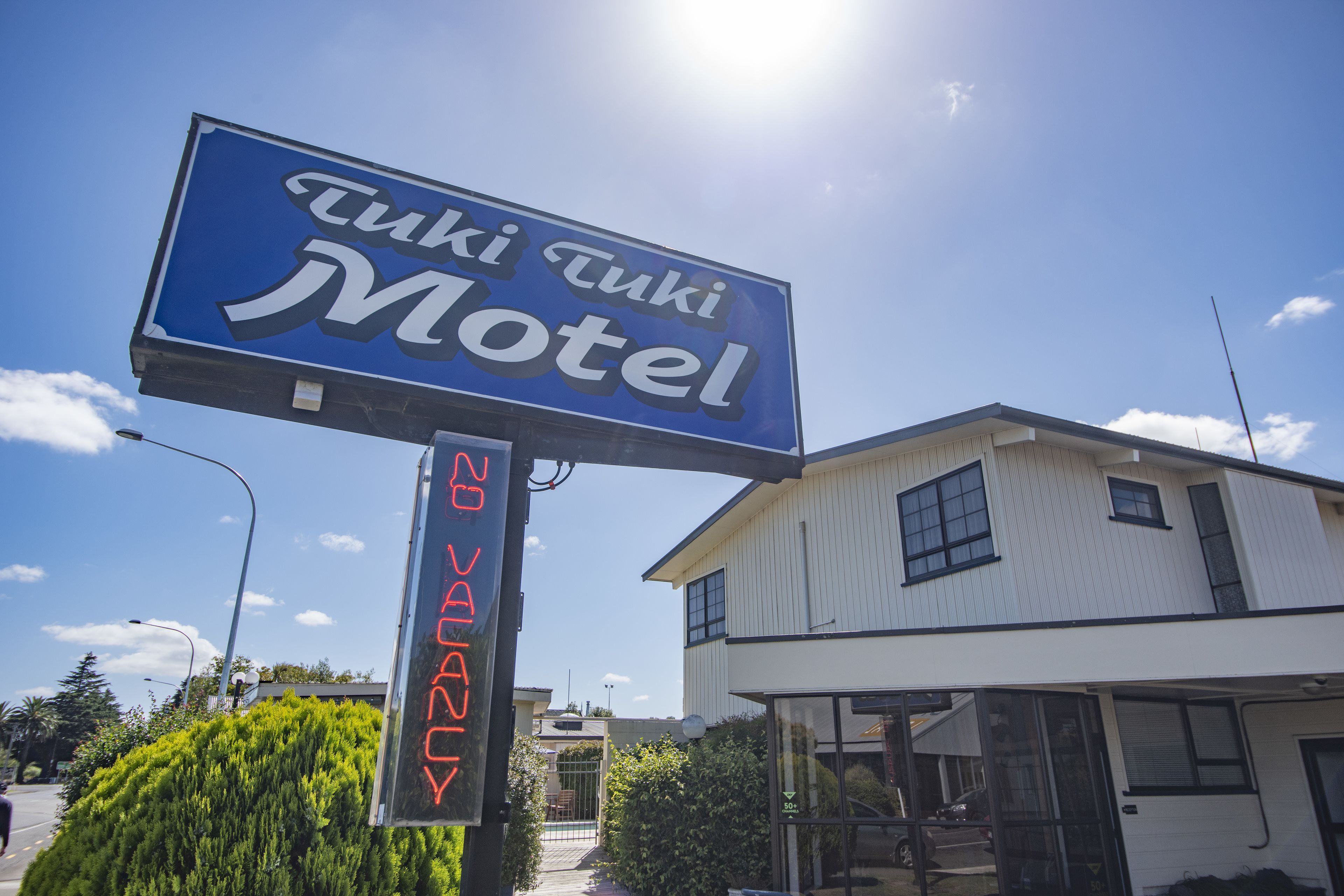 Placa de motel com o nome 'Tuki Tuki Motel' e um letreiro de neon abaixo indicando 'Aberto 24 horas'.