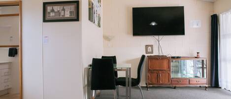 A living room with a flat-screen TV, a dining table with chairs, a cabinet, and a framed picture on the wall.