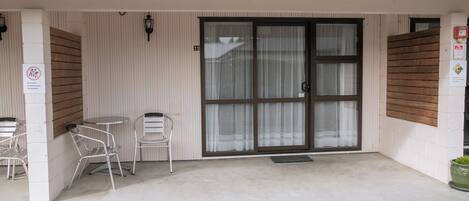 Un espace extérieur abrité avec des chaises et une table en métal, une porte-fenêtre coulissante et un extincteur fixé au mur.