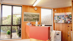 A reception desk with a clock, a framed landscape painting, and a wall with travel brochures. - Tuki Tuki Motel (Waipukurau)