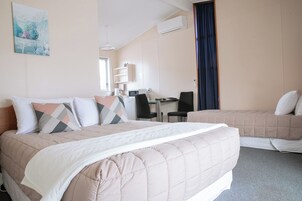 Quarto de hotel com cama, escrivaninha, cadeira e janela com cortinas.