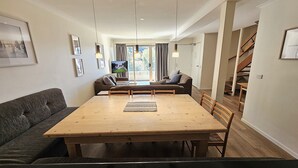 Een eethoek met een houten tafel en stoelen, een bank en een televisie op de achtergrond.
