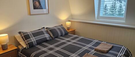A bedroom with a bed, two bedside tables, a window, and a framed picture on the wall.