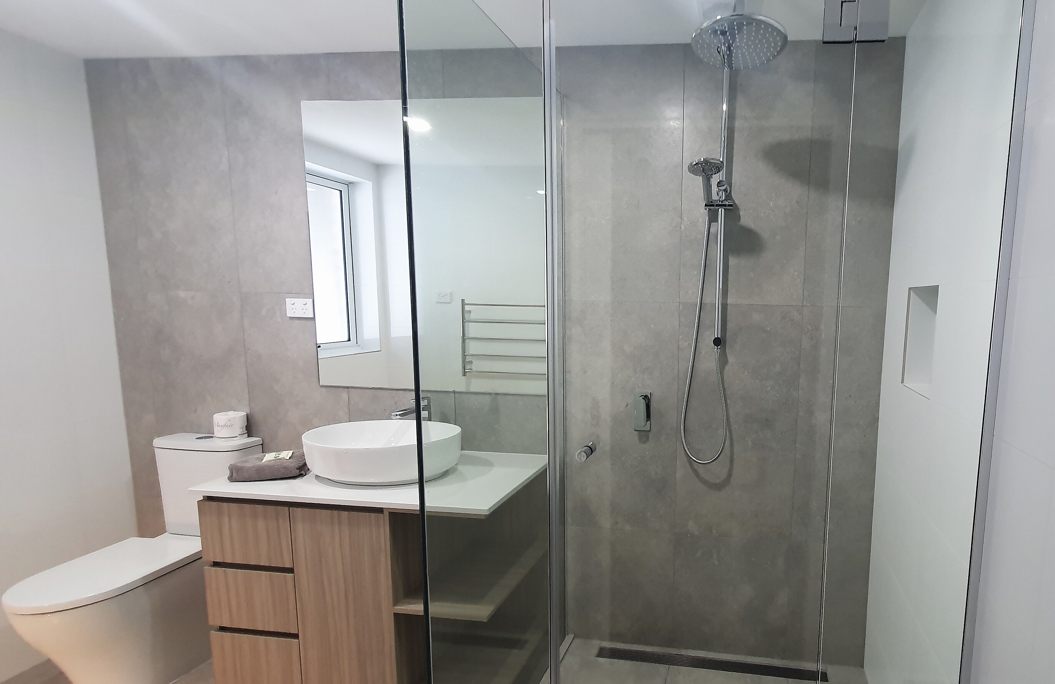 Un baño moderno con ducha de vidrio, un lavamanos blanco y un mueble de madera.