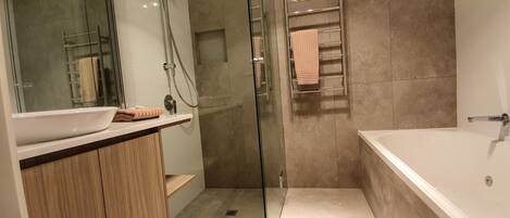 Ein modernes Badezimmer mit einer gläsernen Duschkabine, einem Holzwaschtisch, einer großzügigen Badewanne und einem Handtuchhalter.