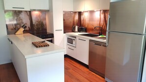 Een moderne keuken met witte kastjes, een centraal eiland, een roestvrijstalen koelkast en een houtgestookte kachel.
