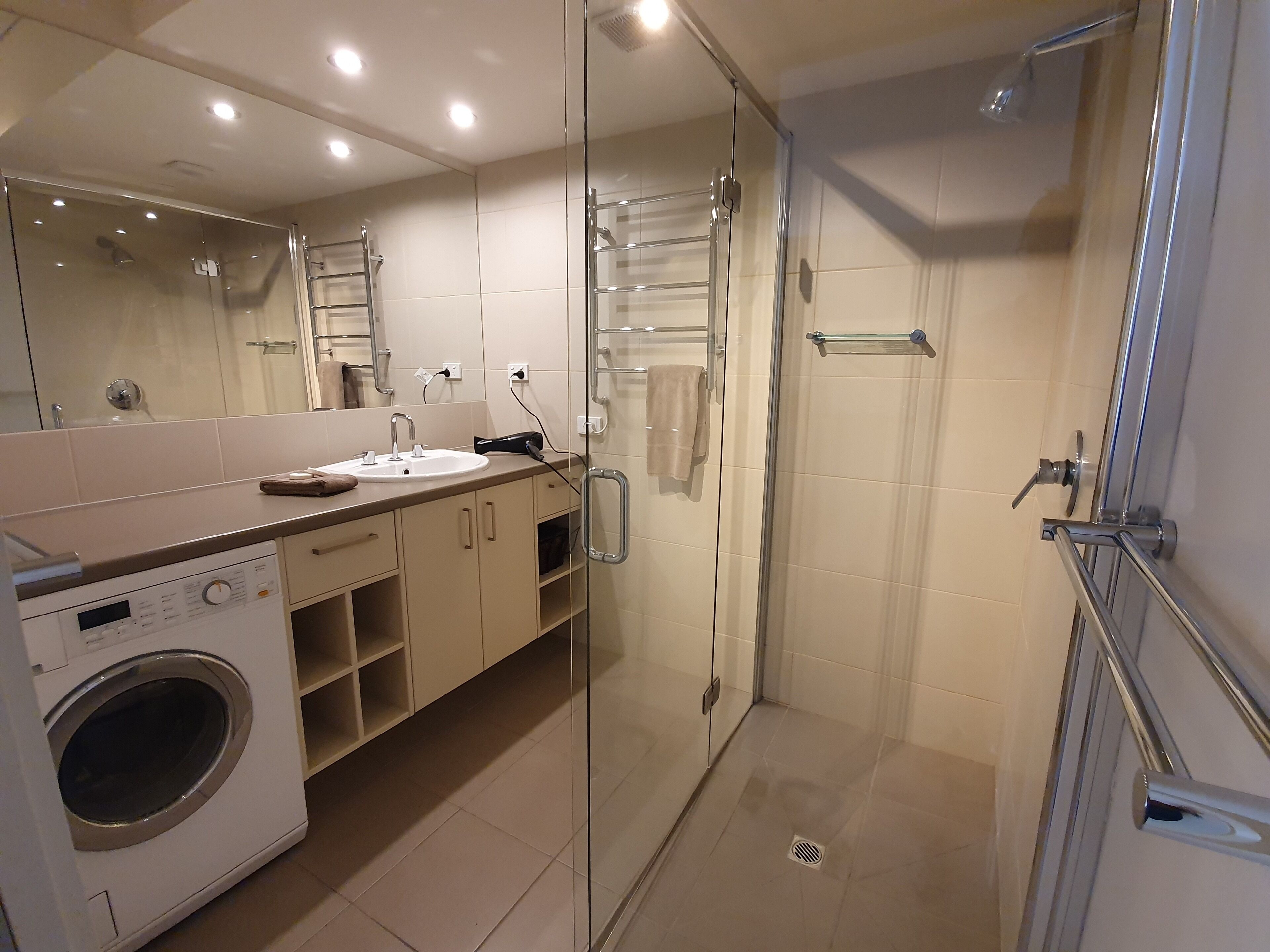 Un baño moderno con cabina de ducha de vidrio, lavadora integrada y un espejo grande.