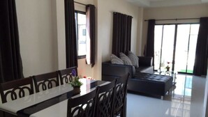 Un salon moderne avec un coin repas, comprenant un ensemble de canapés, une table à manger avec des chaises et de grandes fenêtres avec des rideaux.