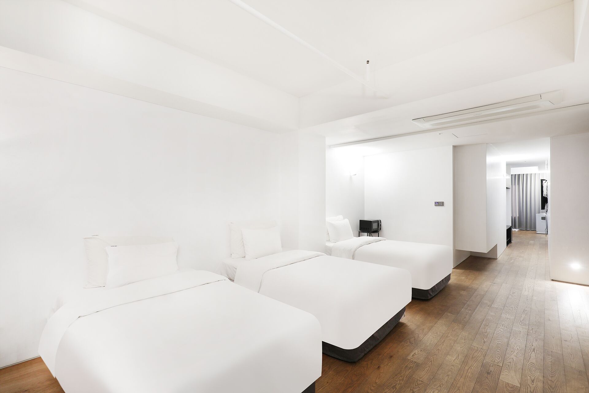 Una habitación de hotel moderna con dos camas individuales, un televisor de pantalla plana y piso de madera.