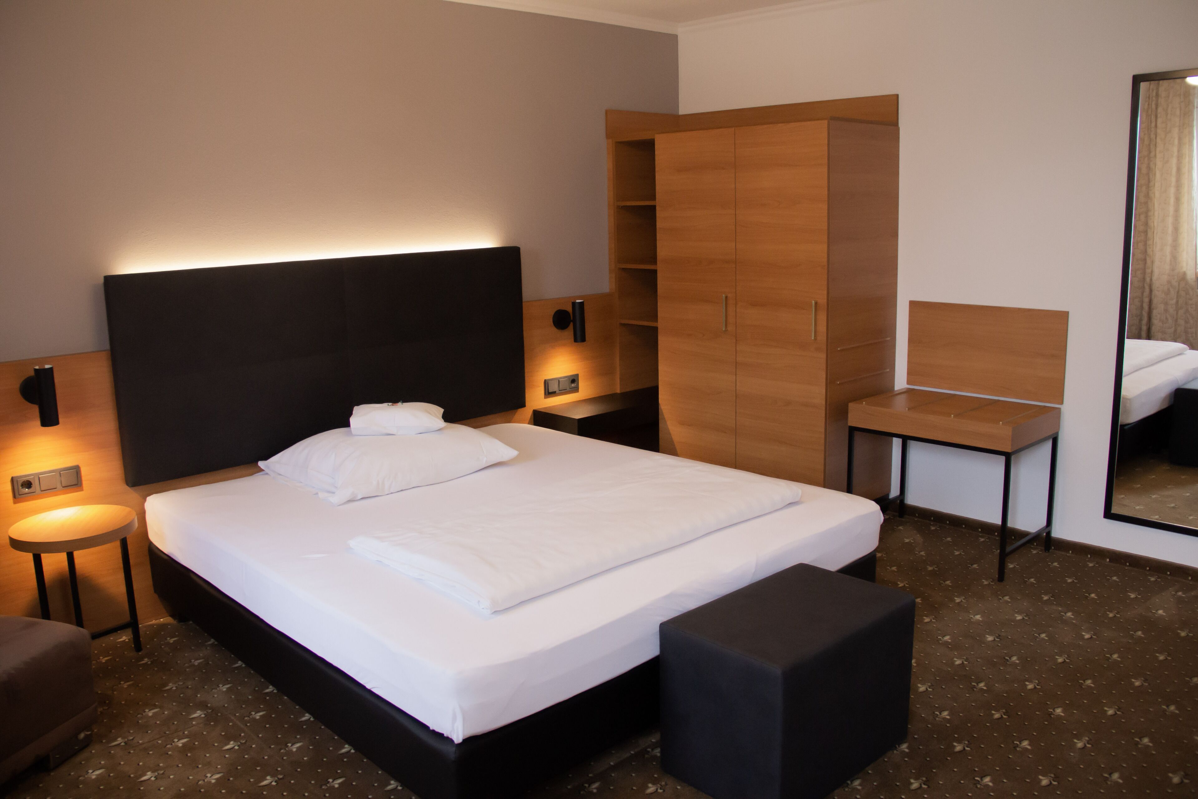 Ein Hotelzimmer mit einem großen Bett, einem Holzschrank, einem Nachttisch und einem Spiegel.