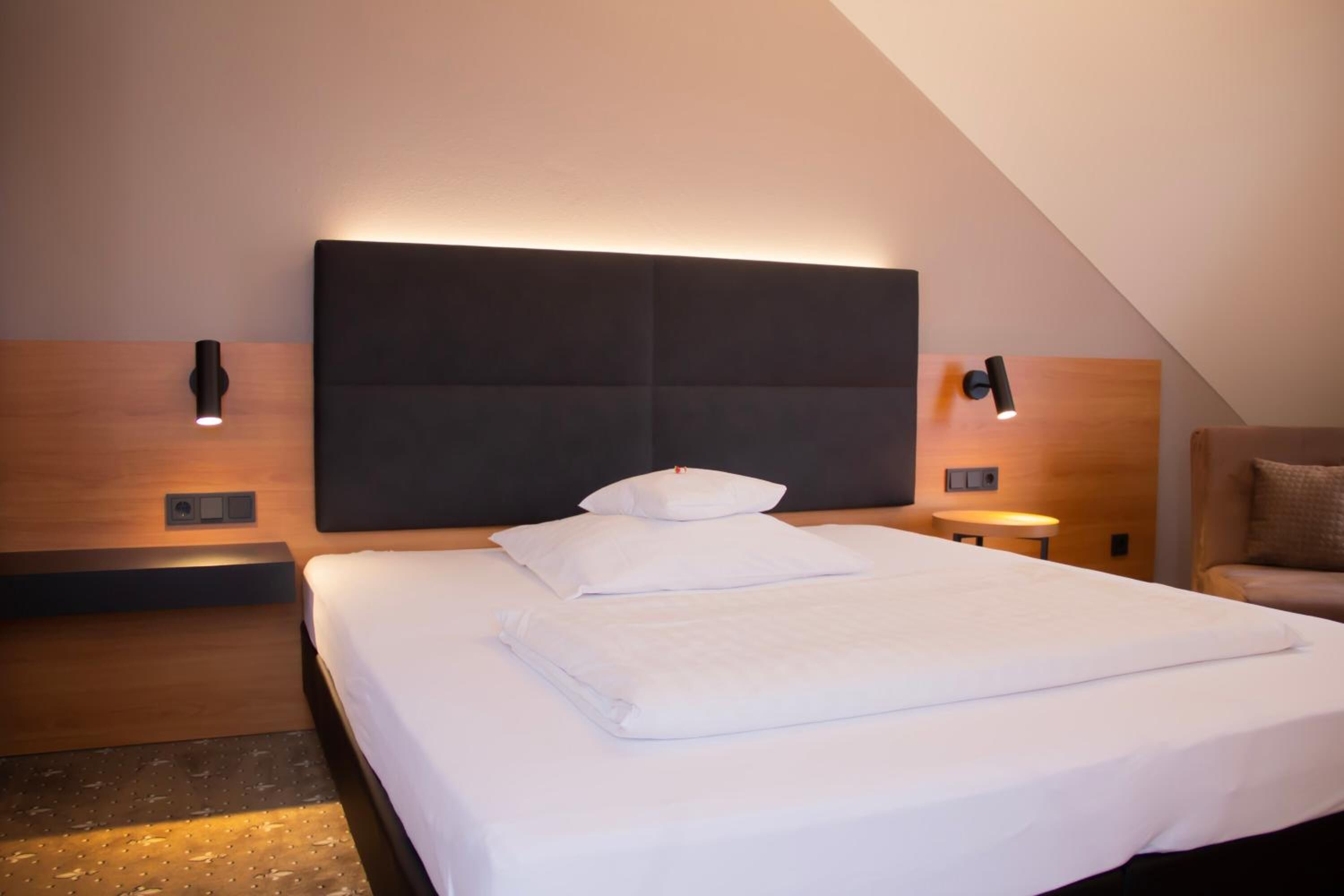 A neatly made bed with white linens in a modern hotel room.