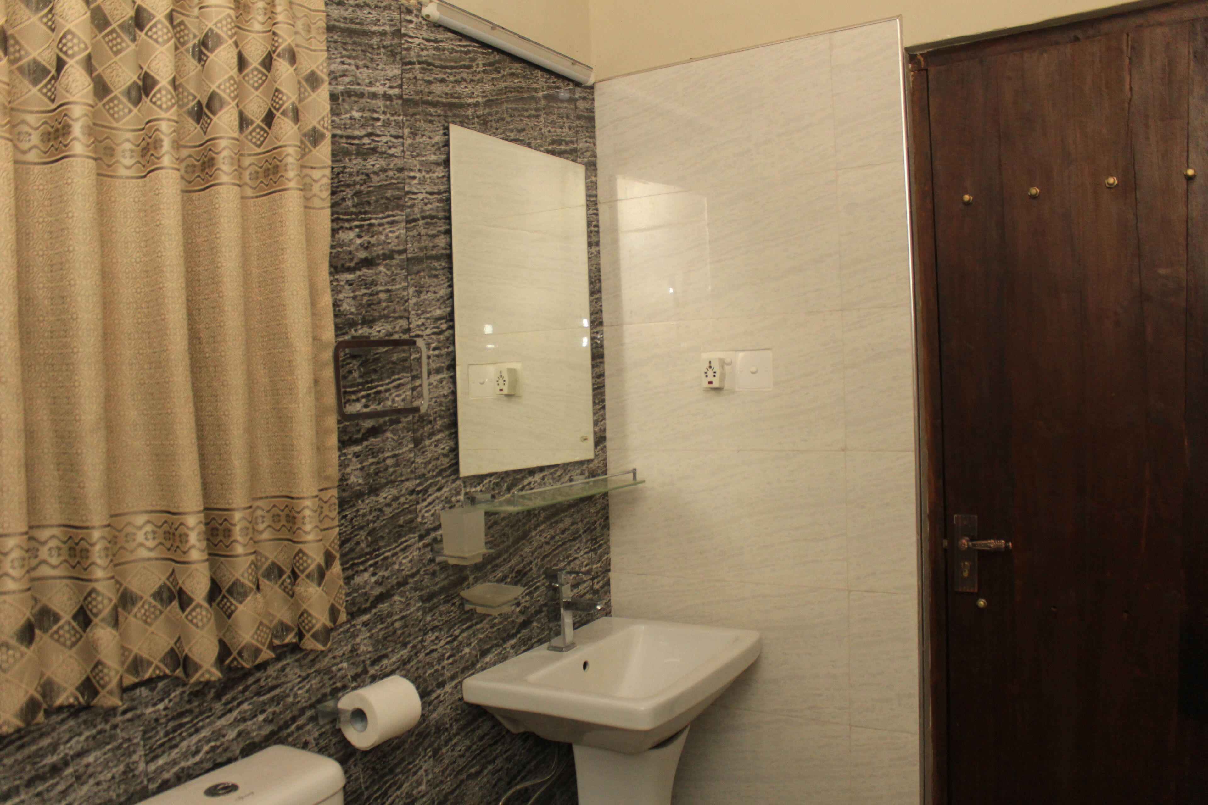 A bathroom with a marble wall, a sink, a mirror, a towel, and a wooden door.