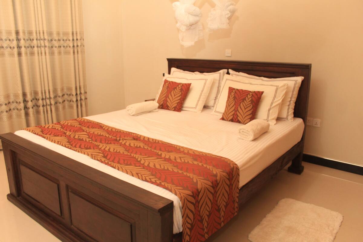 A neatly made bed with a patterned bedspread and pillows, a wooden headboard, and a white rug on the floor.