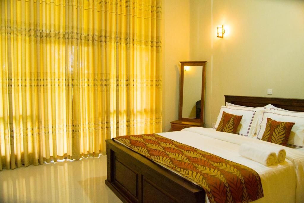 A hotel room with a bed, curtains, a nightstand, a mirror, and a wall-mounted light.