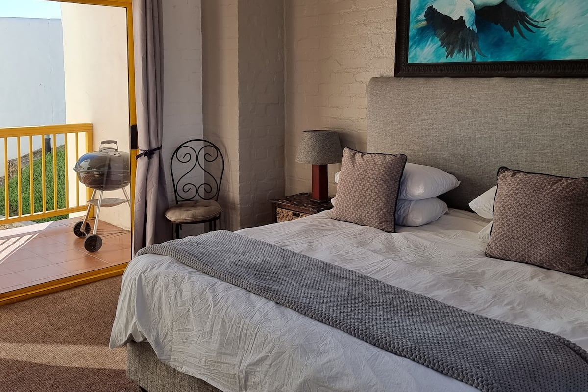 A bedroom with a large bed, a chair, a lamp, and a painting of a bird.