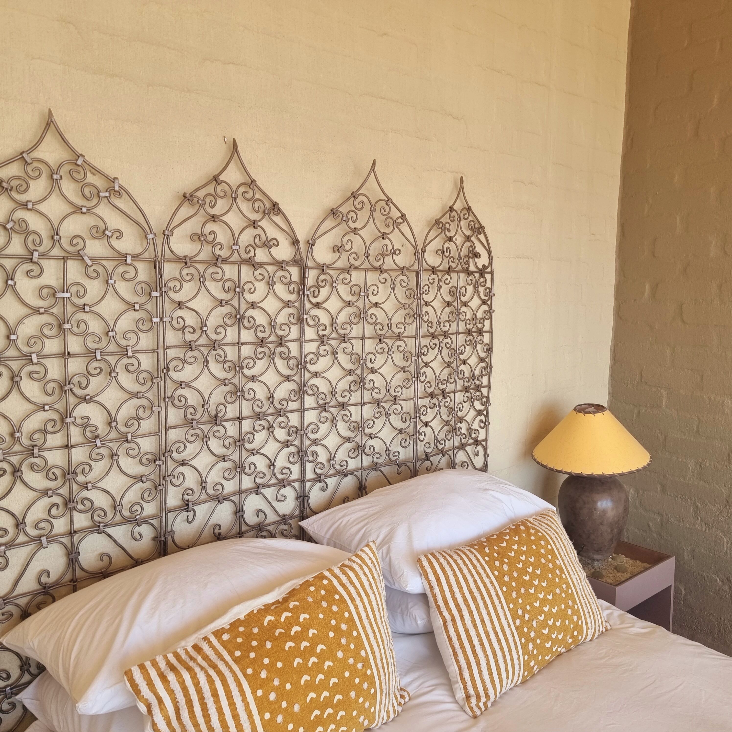A bed with white and striped pillows, a metal headboard with intricate designs, and a lamp on a bedside table.