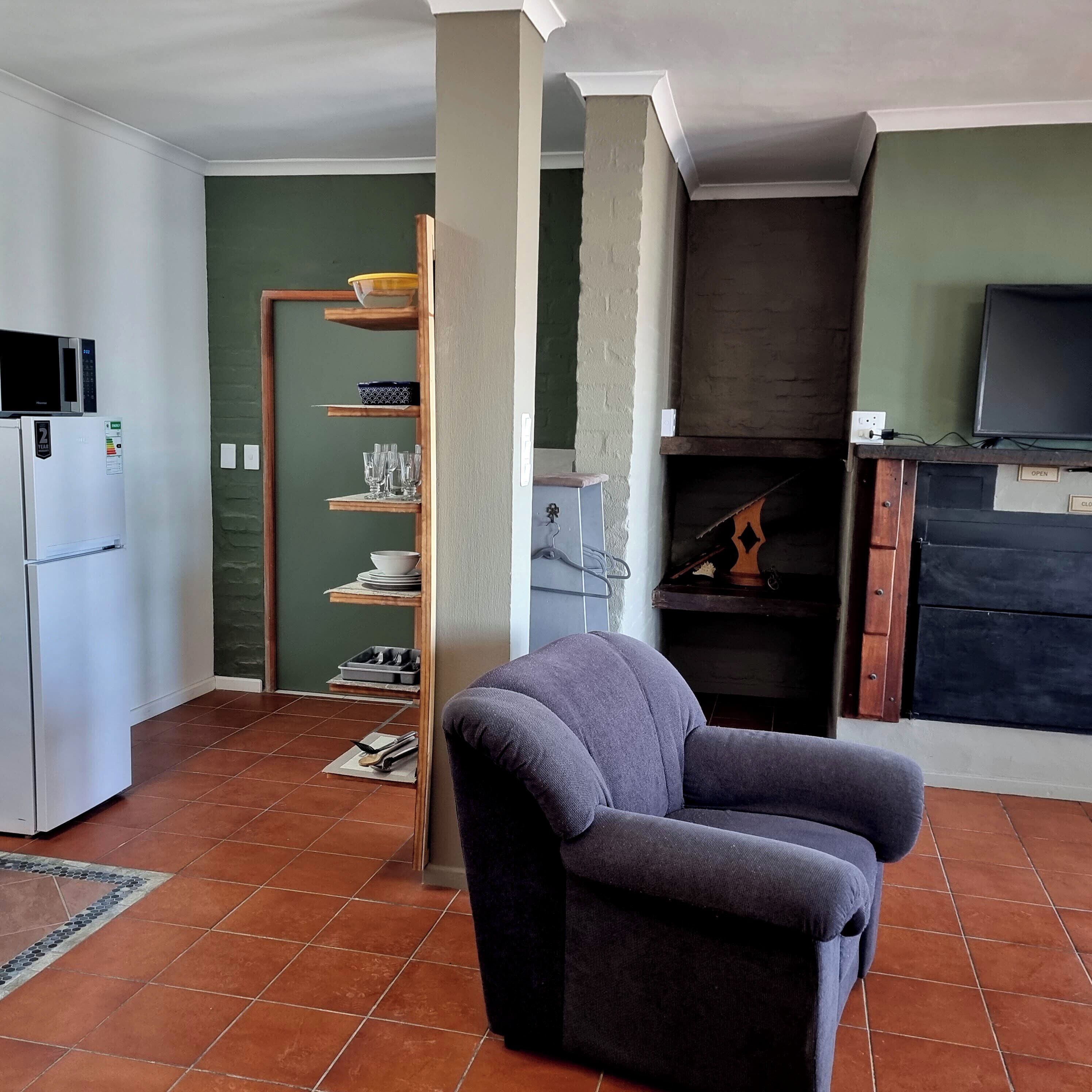 A compact living space with a kitchenette, a grey armchair, and a television.