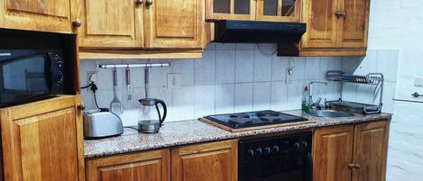 A kitchen with wooden cabinets, a microwave, a kettle, a toaster, a stove, and a dishwasher.