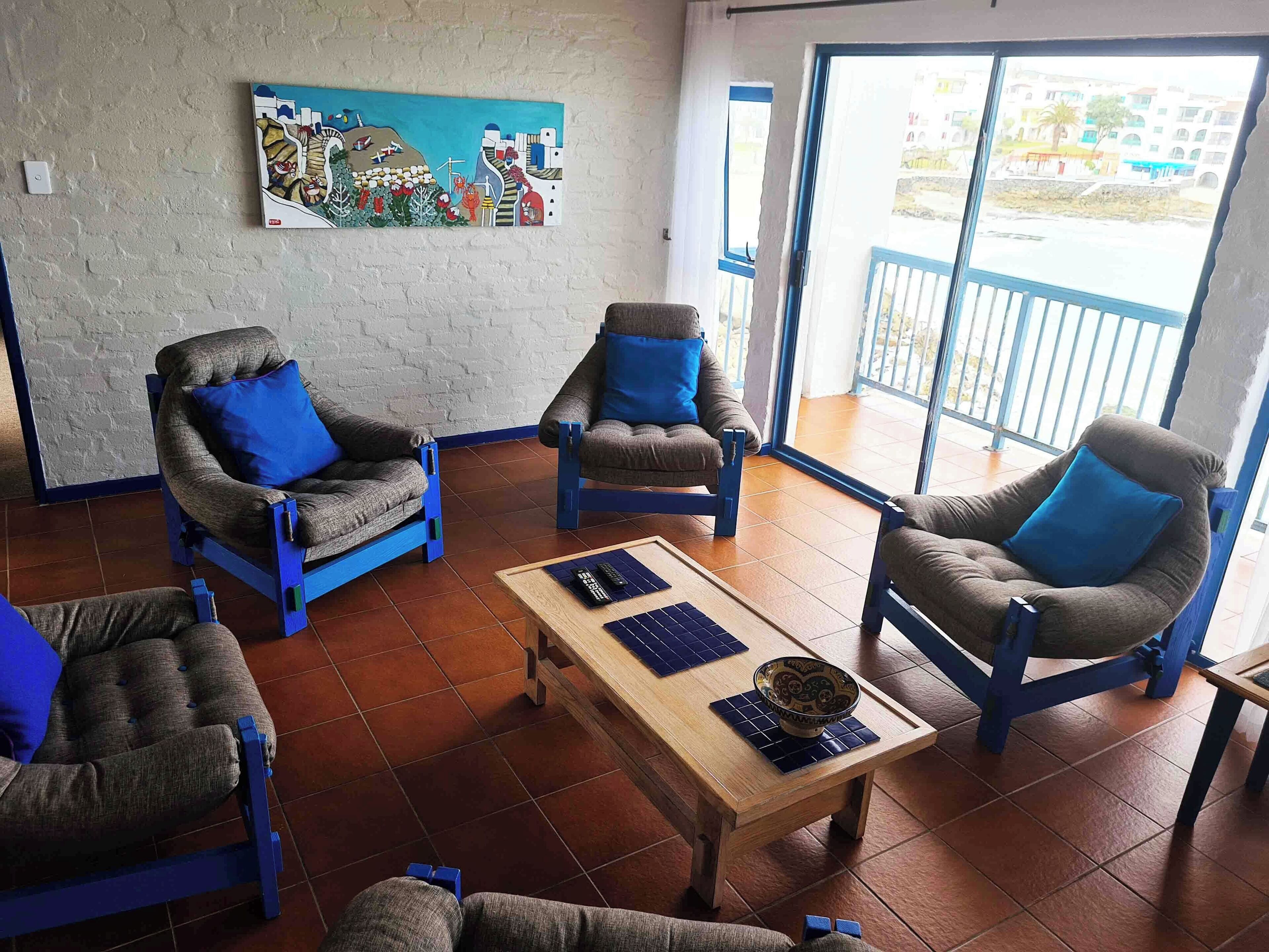 Uma sala de estar com quatro poltronas, uma mesa de centro e um quadro na parede.