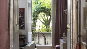 A narrow hallway with a staircase leading to a balcony, a door with a mirror, and a view of greenery outside. - Luxury Design Hotel Particulier le 28 (Aix-en-Provence)