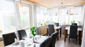 Un comedor con mesas dispuestas para cuatro, sillas y plantas en macetas.