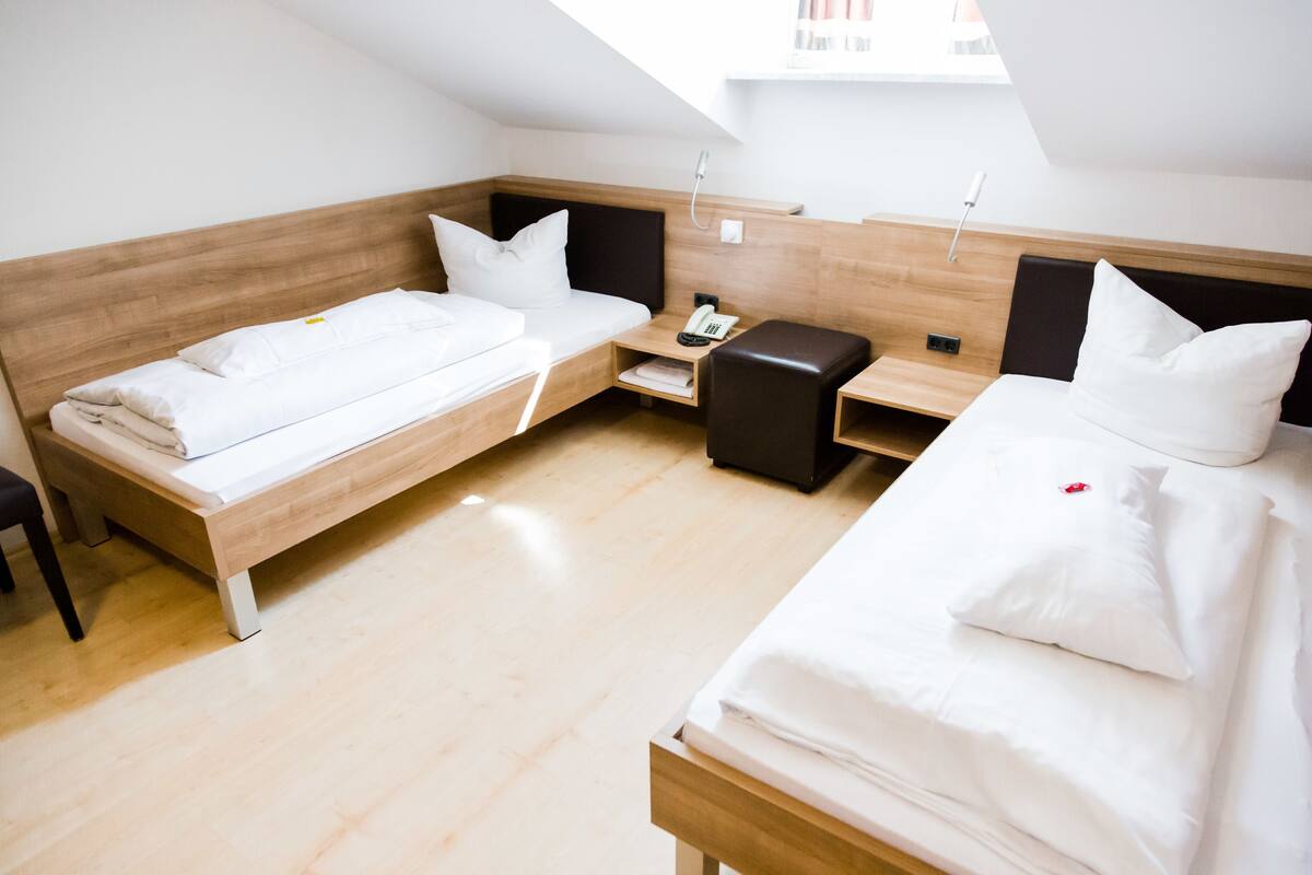 A modern hotel room with two single beds, a small desk, a chair, and a bedside table with a phone.
