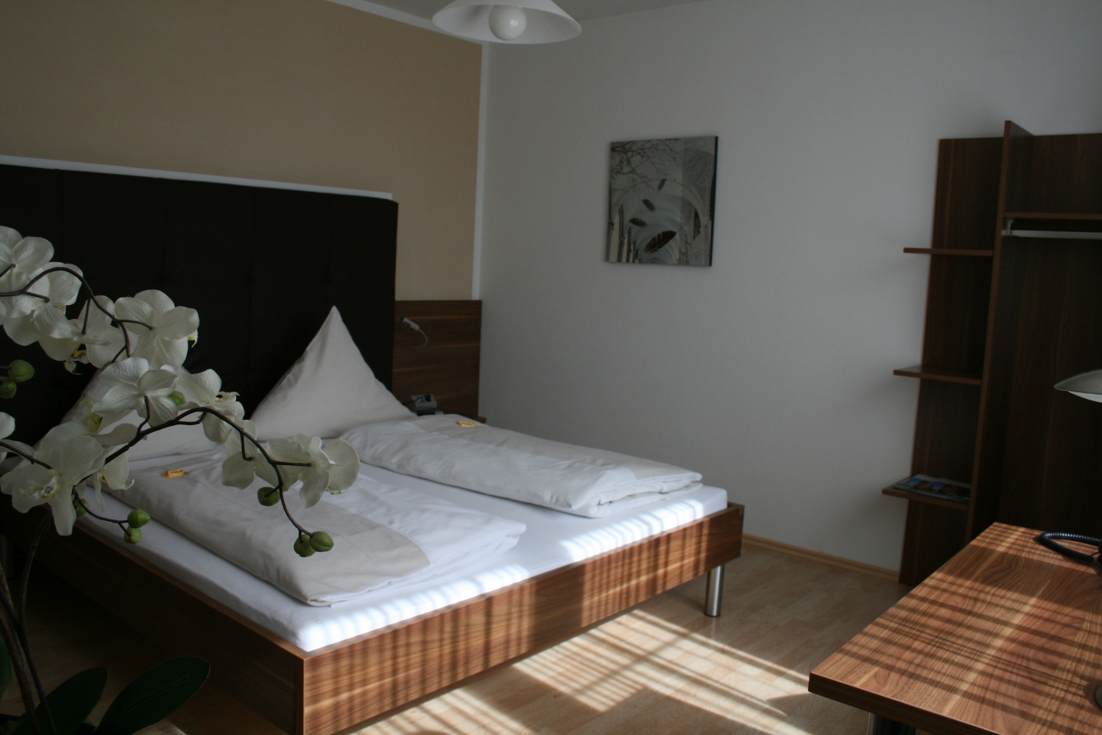 A neatly made bed with white linens, a wooden headboard, and a bedside table with a lamp.