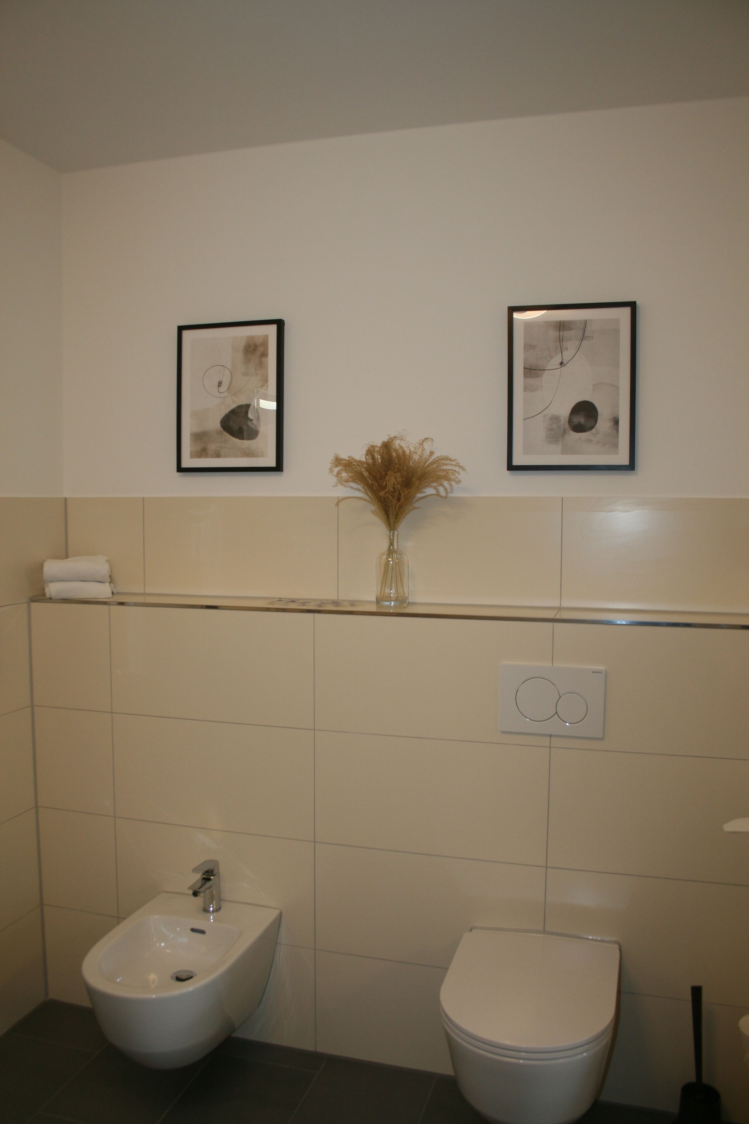 A bathroom with a bidet, toilet, and two framed pictures on the wall.