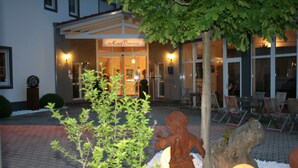 A hotel entrance with a sign reading "Hotel Tavares," outdoor seating, and a statue of a child. - Hotel Bavaria Garni (Dingolfing)