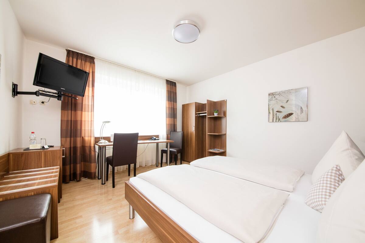 A hotel room with a bed, desk, chair, and a TV mounted on the wall.