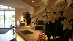 A reception area with a marble counter, a vase of white orchids, and a view of the outdoors through glass doors. - Hotel Bavaria Garni (Dingolfing)