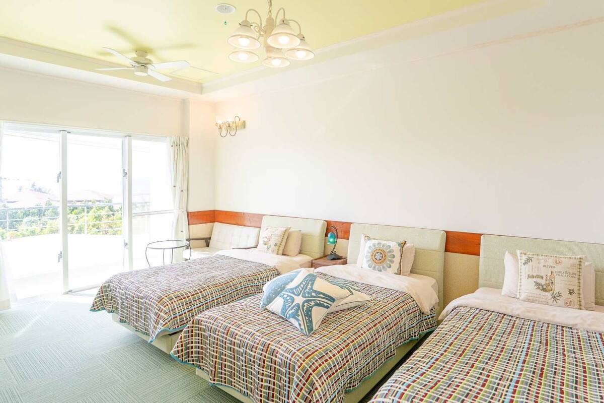 A hotel room with two beds, a ceiling fan, a small table, and a view of the outdoors.