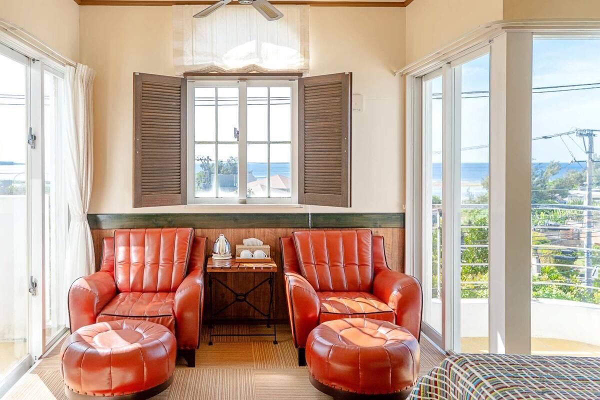 A balcony with two leather chairs, a small table with a kettle, and a view of the sea.