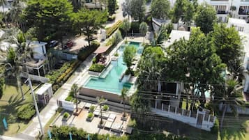 An aerial view of a residential area with a swimming pool surrounded by lush greenery and palm trees.