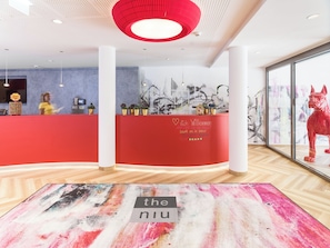 A reception area with a red counter, a receptionist, and a large window with a cityscape view. - niu Franz (Wien)