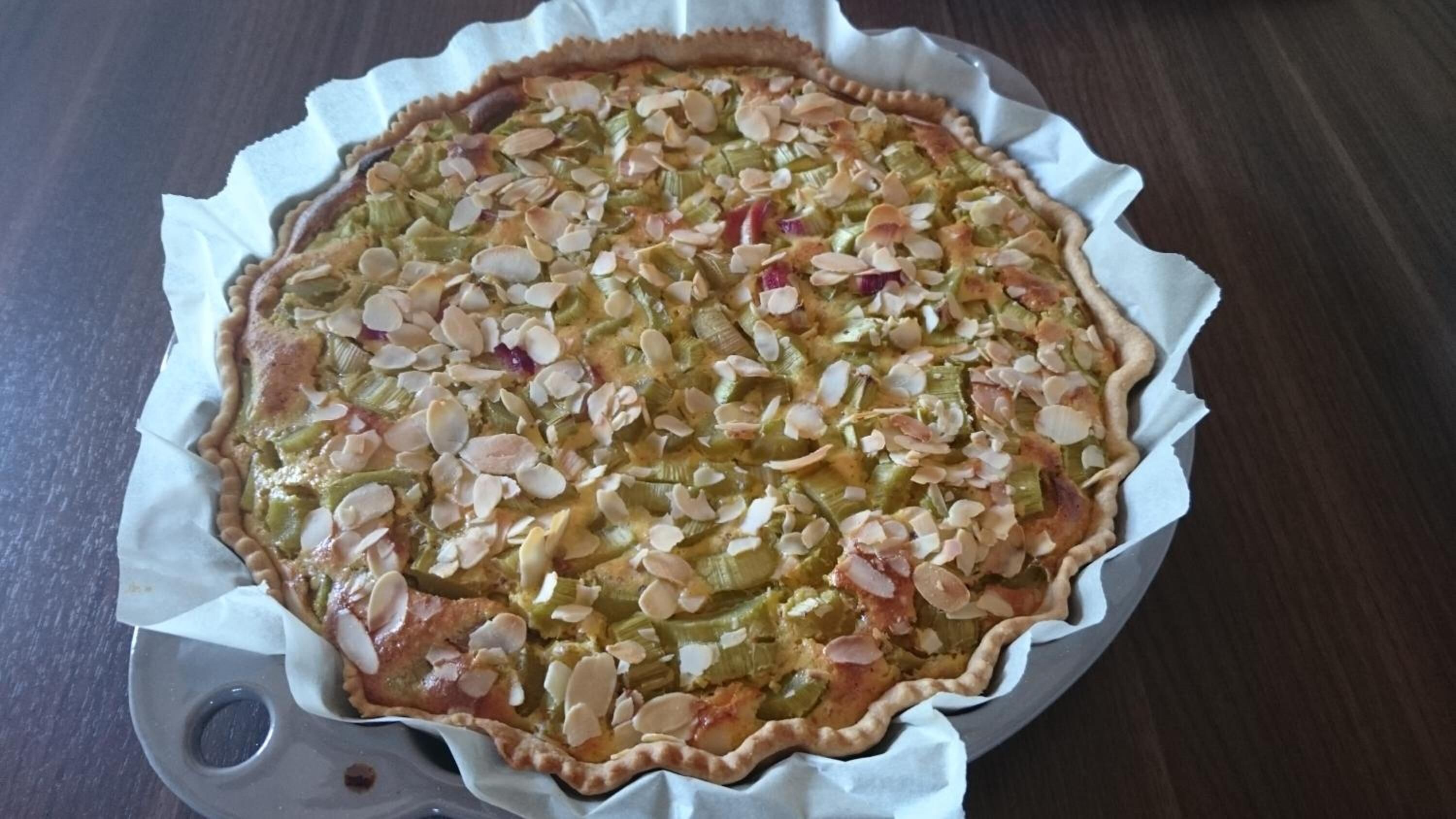 A pie with sliced almonds on top, placed in a pie dish on a wooden surface.
